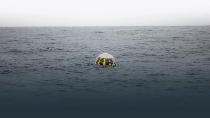 A small, half-submerged yellow oval device with solar panels in a transparent dome floats in the ocean