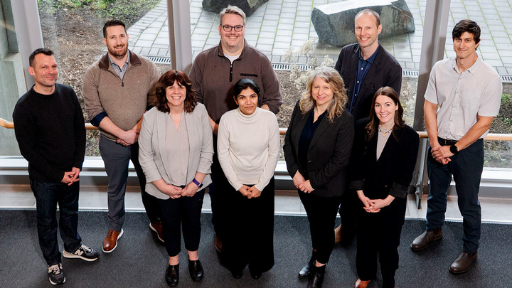 Nine members of the ACET team stand smiling in a semi-circle facing the photographer