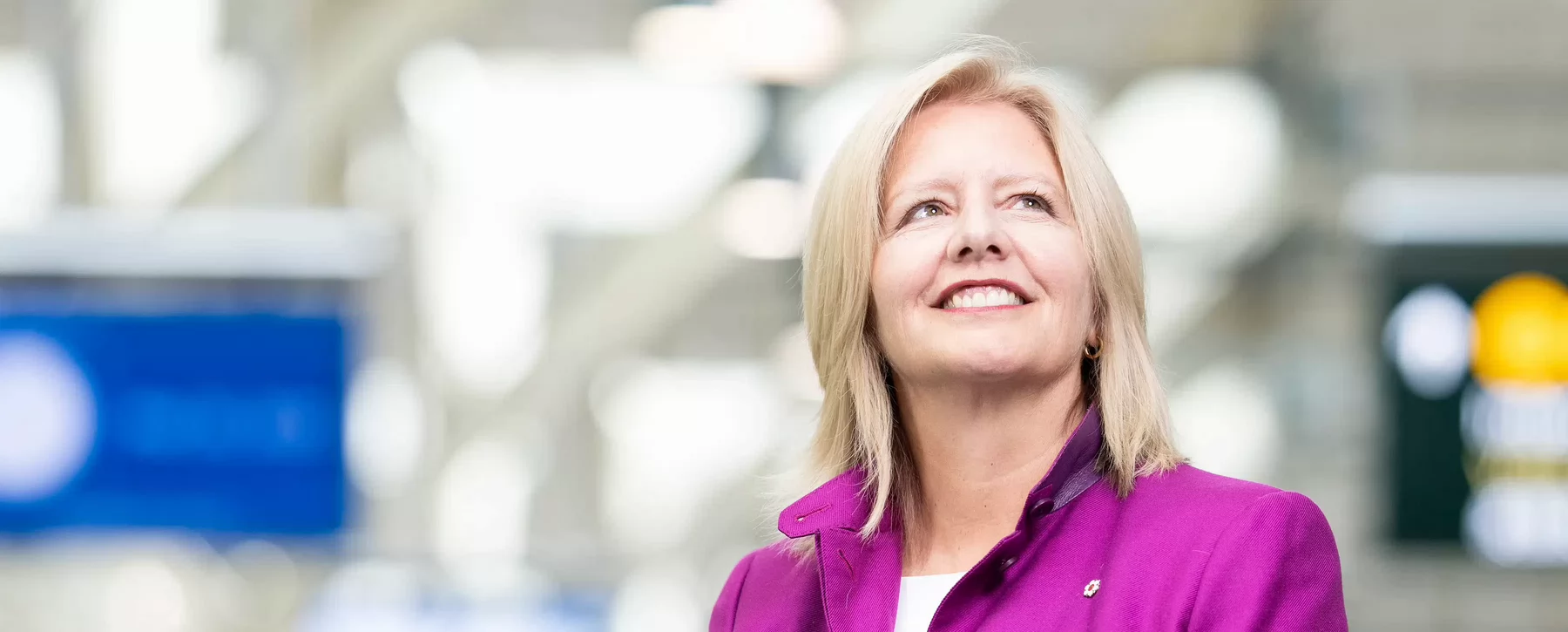 Woman with shoulder length hair in an airport terminal smiling while looking upwards.