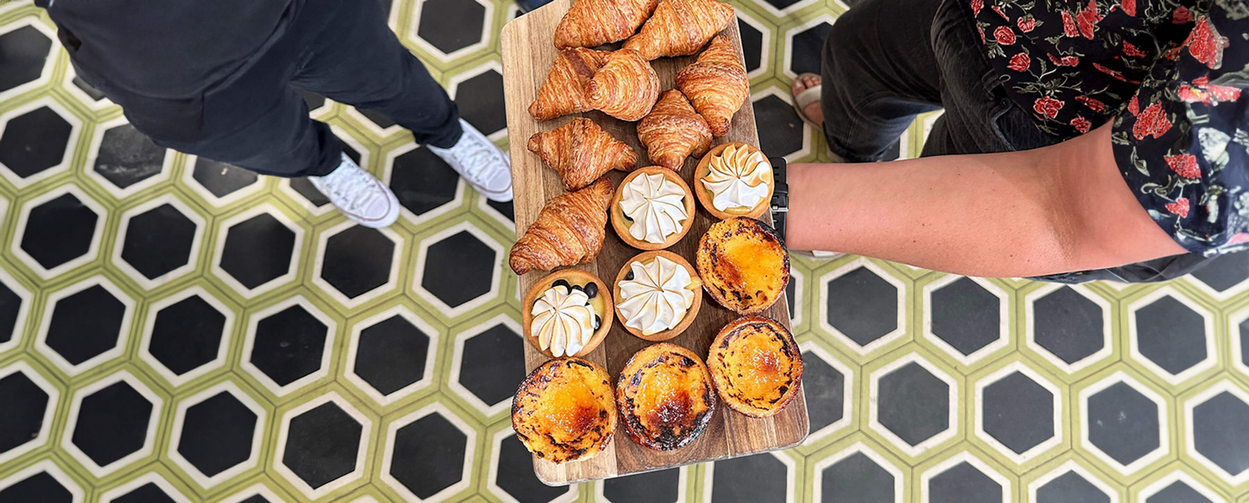 Person in flowery shirt holding a bread board covered in pastries. 
