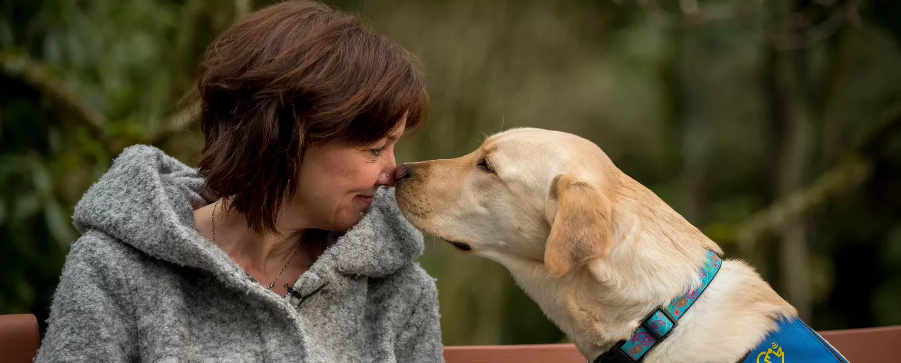 A woman touching noses with an assistance dog.