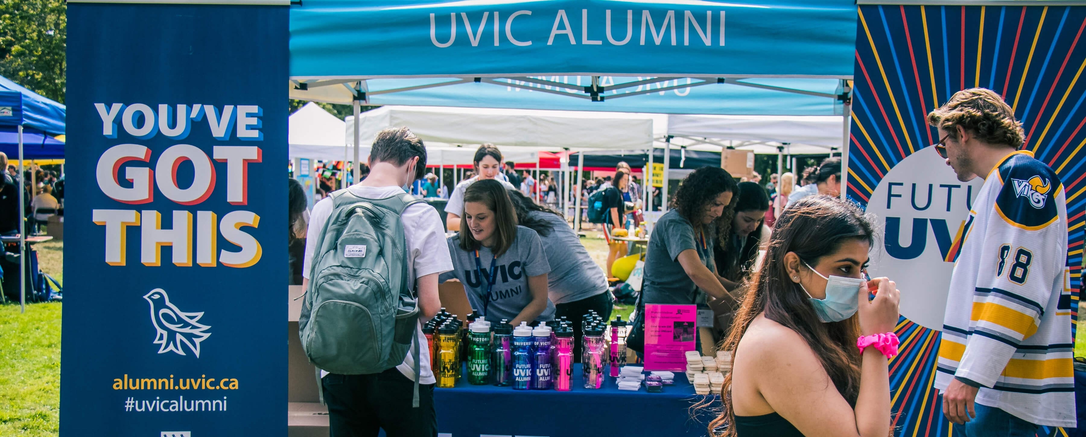 Students gathering outdoors around a UVic alumni kiosk