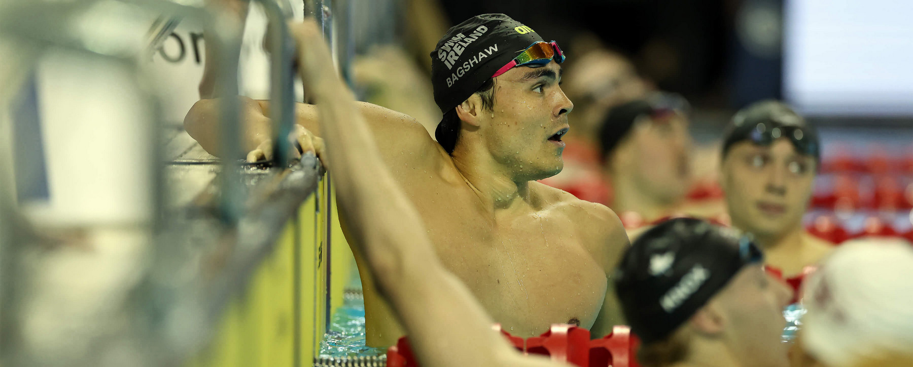 Man in swim cap and swim goggles in a pool looking upwards at end of a race.