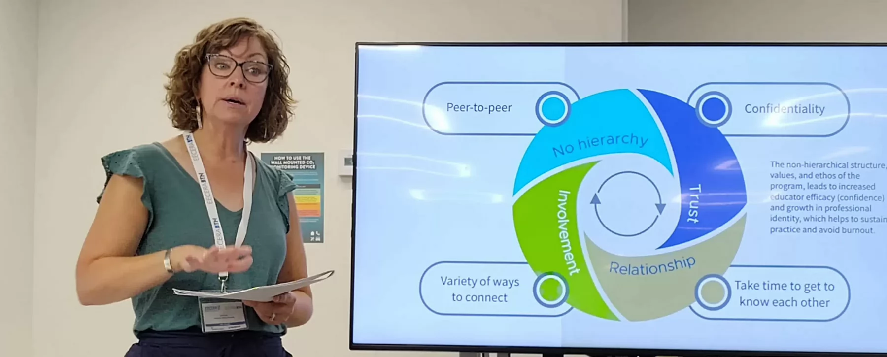 A woman with glasses standing beside a screen delivering a Power Point presentation..