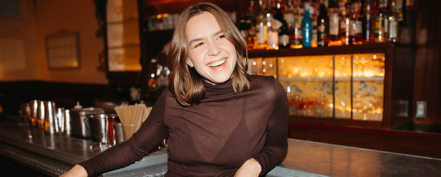 Woman smiling while leaning against a bar. 