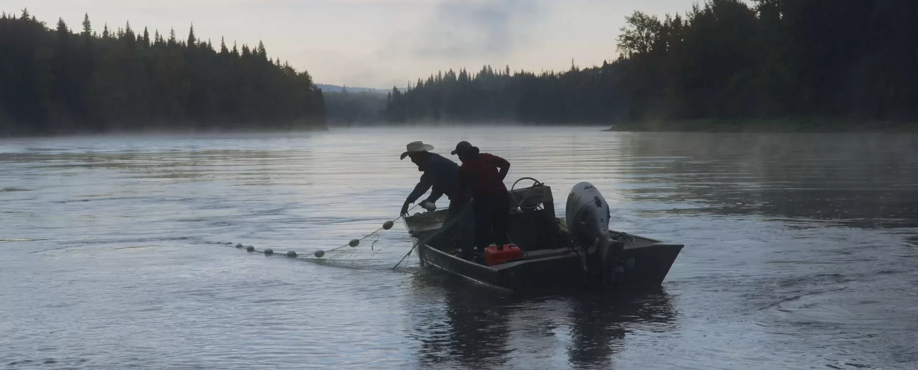 Two people in an aluminum boat floating on a river haul in fishing nets.