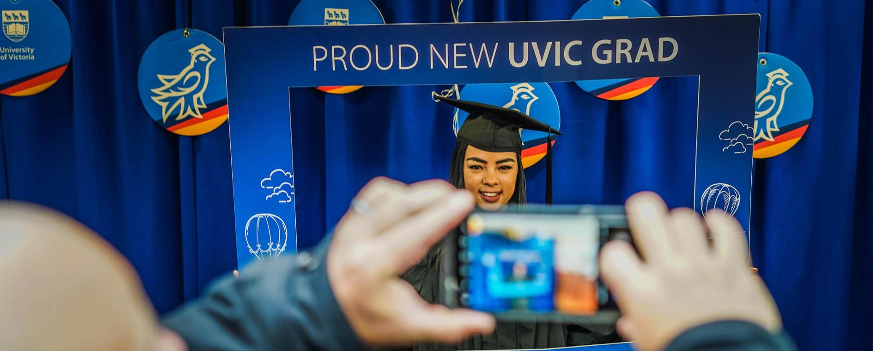 Grad in cap and gown posing in cardboard blue instagram frame