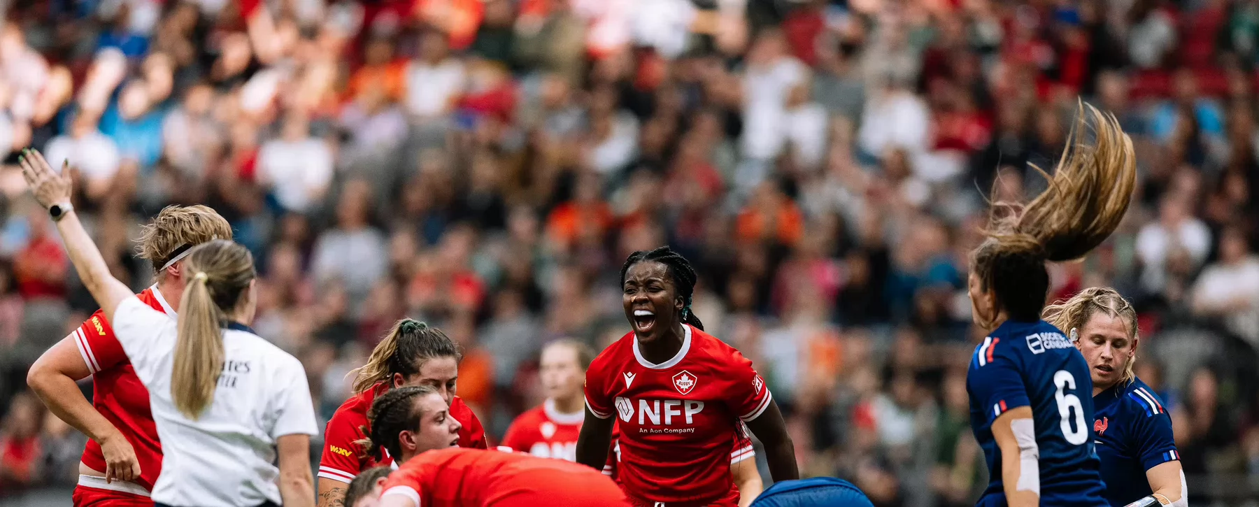 A Canadian women's rugby team player in a scrum of players yelling while an official raises her arm in the air. 