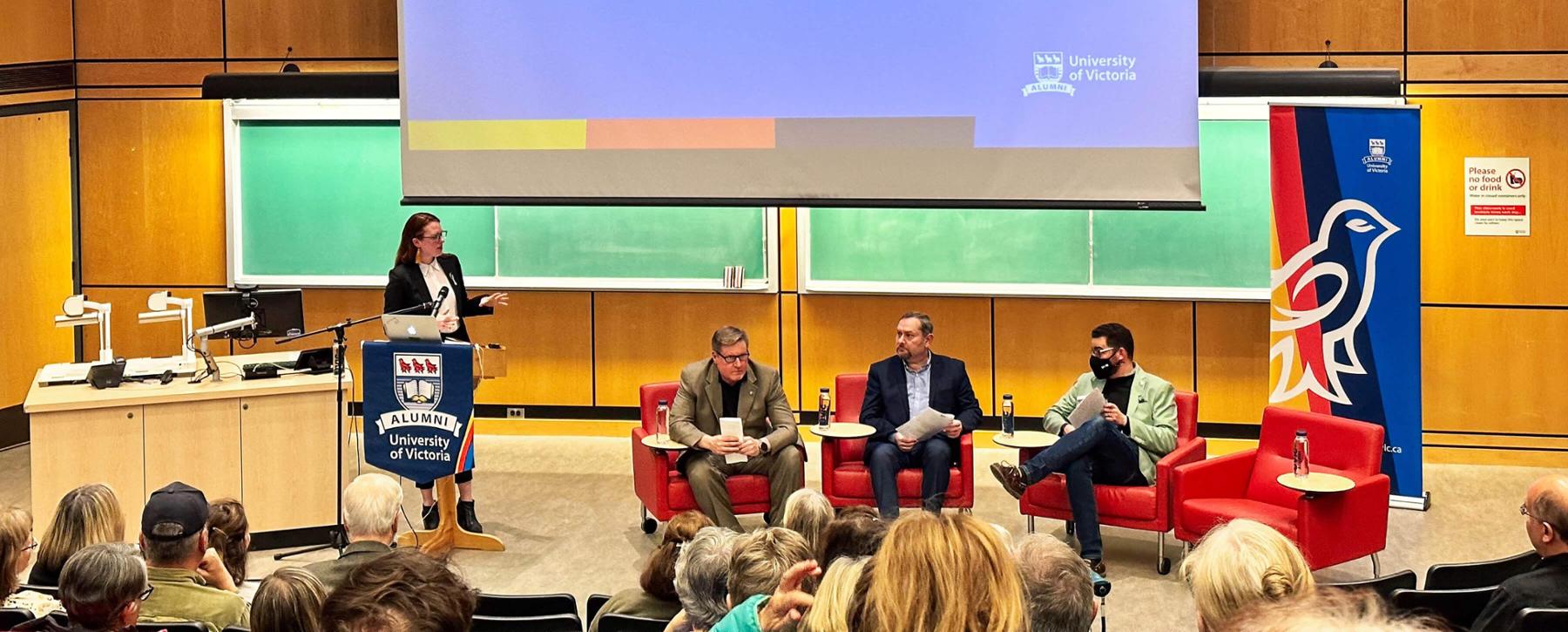Panel discussion in front of an audience in a small auditorium. 