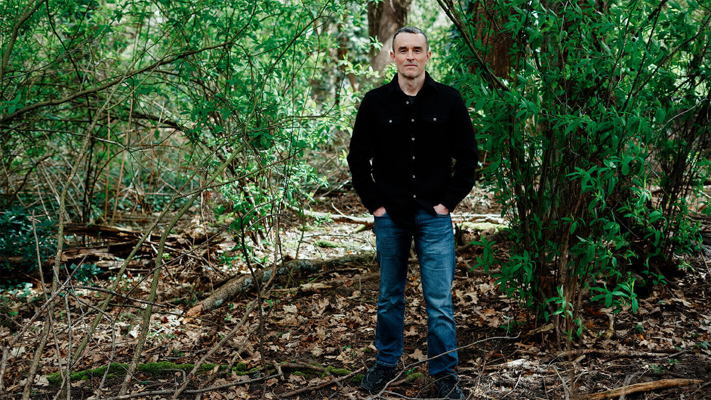 Man standing in the woods with his hands in his pocket. 