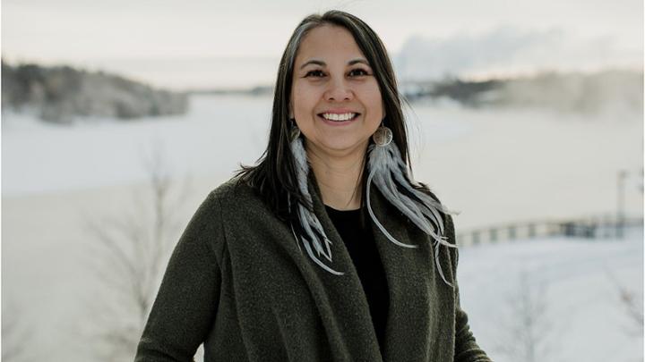 Woman smiling with feather earrings while standing outdoors.