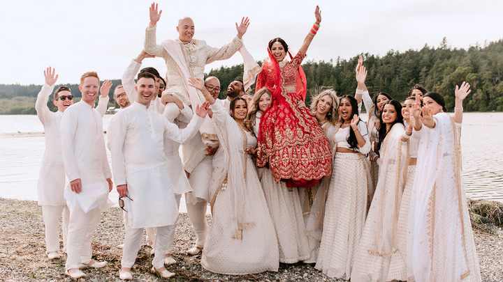 Bride and groom sitting on the shoulders of wedding party with arms raised in the air. 