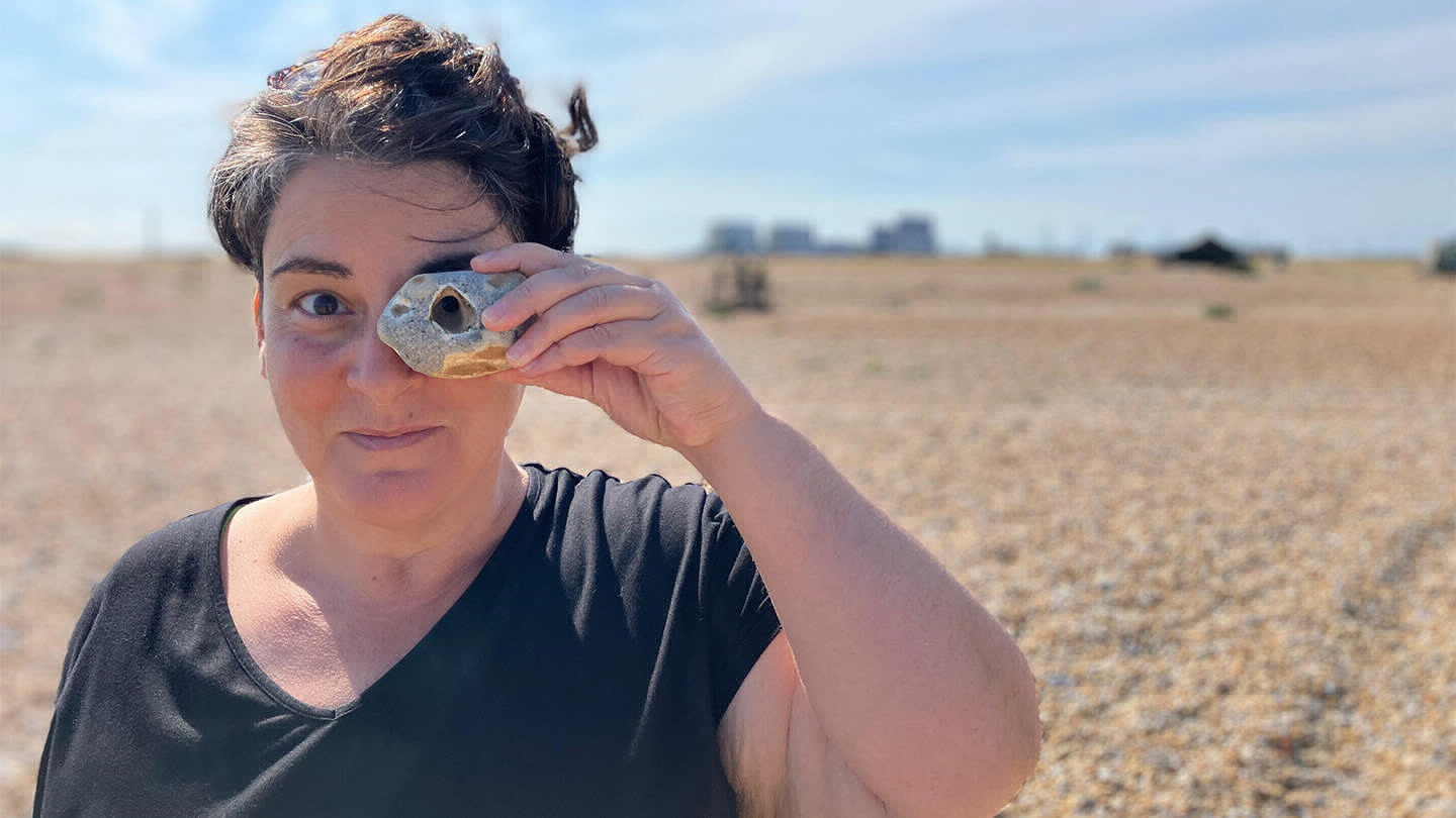 Person standing outside holding a shell or rock with a hole in it up to their eye.