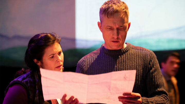 Woman and man standing side by side looking at an unfolded piece of paper. 
