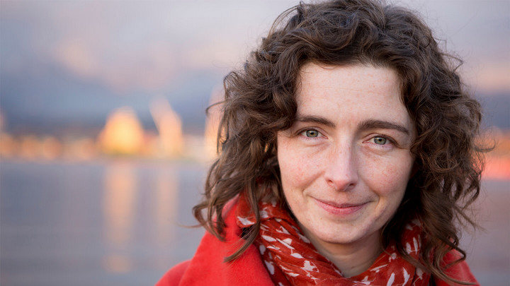 Woman with curly, shoulder length hair wearing a red scarf and red jacket, standing outside.