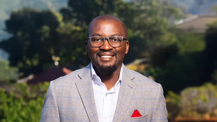 A man with glasses smiling and wearing a blazer with a pocket square.