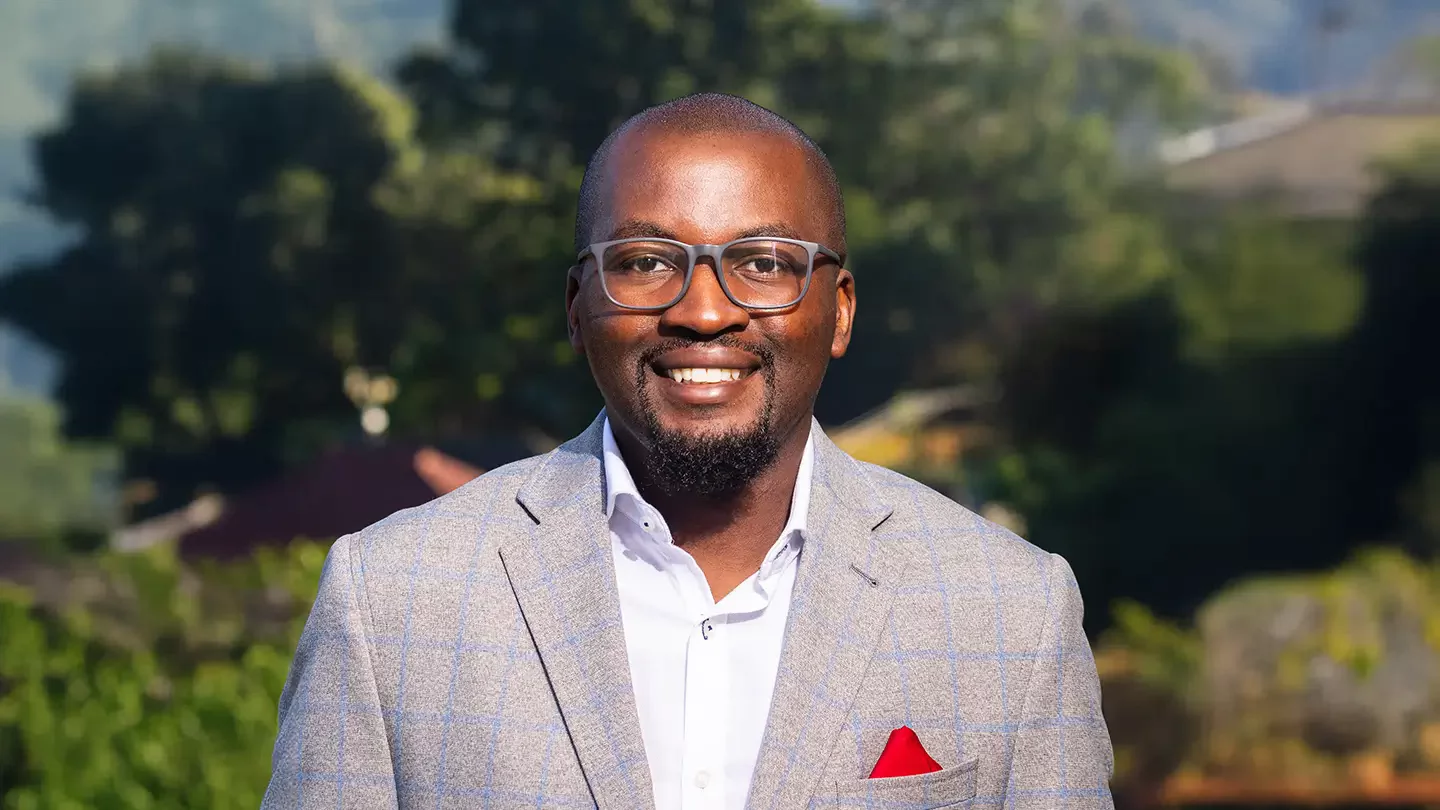 A man with glasses smiling and wearing a blazer with a pocket square.
