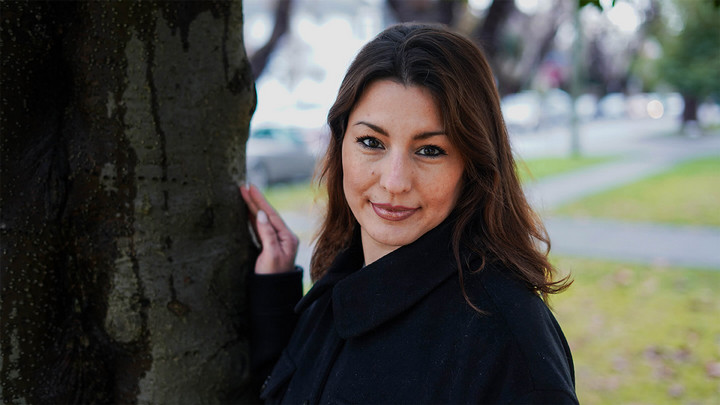 Dark haired woman standing against a tree.