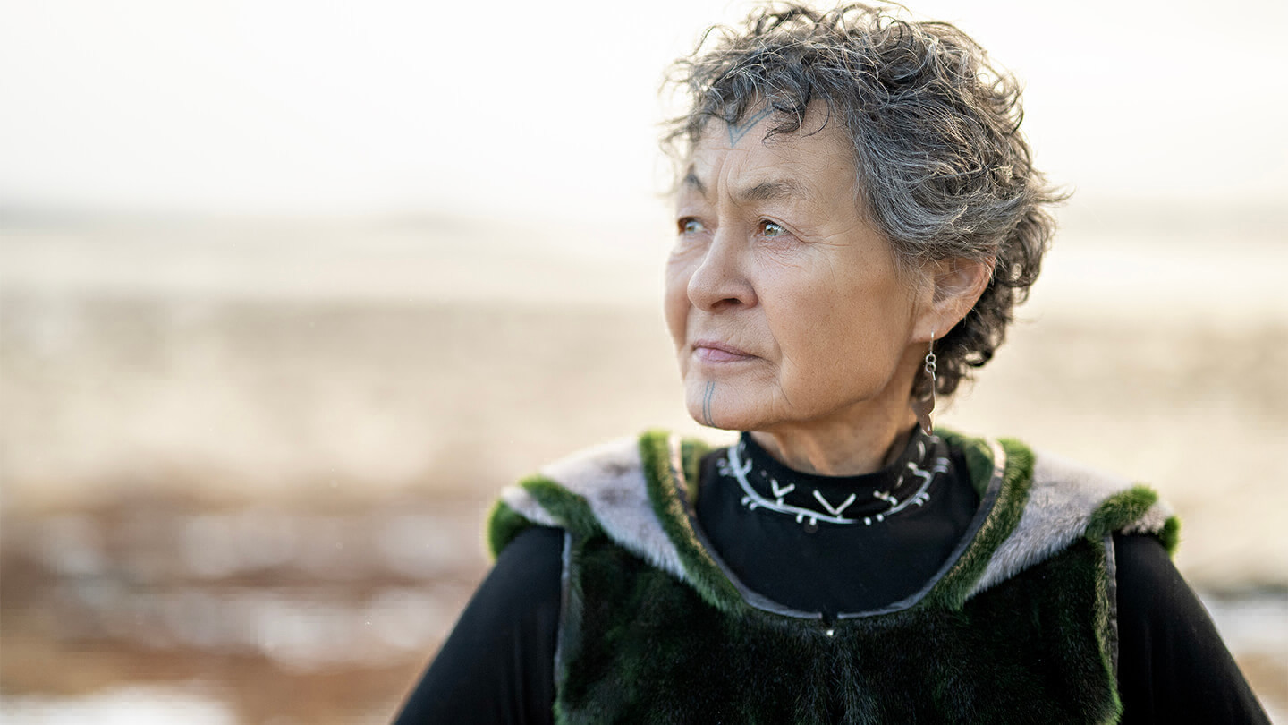 Woman with fur vest and Inuit tattoo marking on her face looking into the distance.