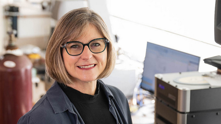 Woman wearing glasses smiling in a science lab.