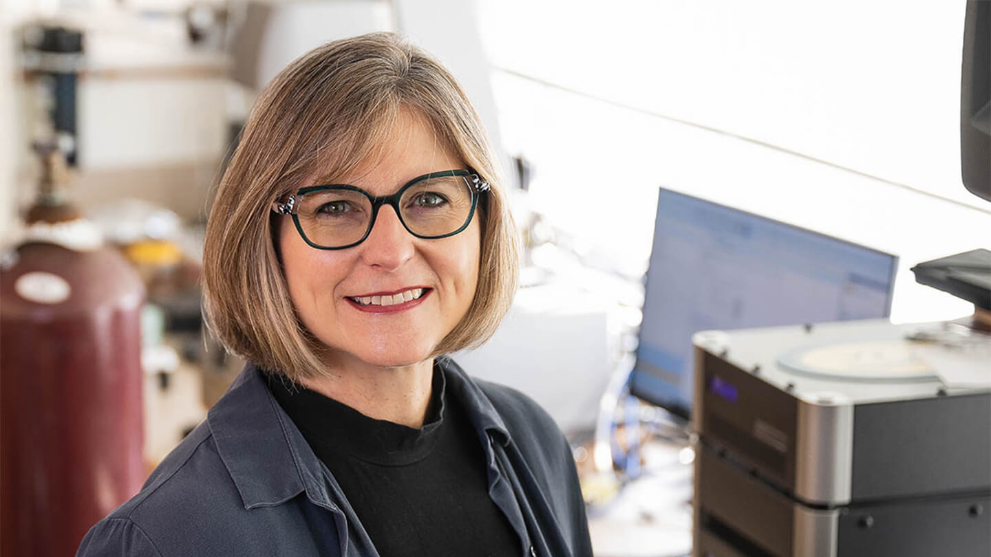 Woman wearing glasses smiling in a science lab. 