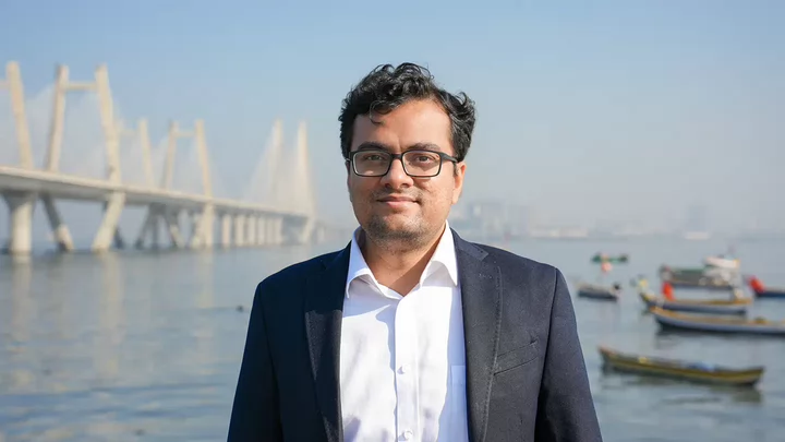 A man with glasses standing in front of a bridge.