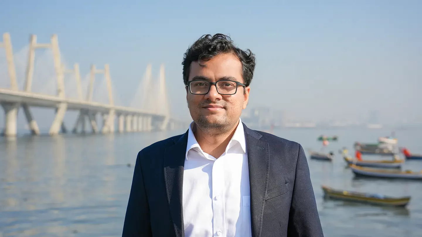 A man with glasses standing in front of a bridge.