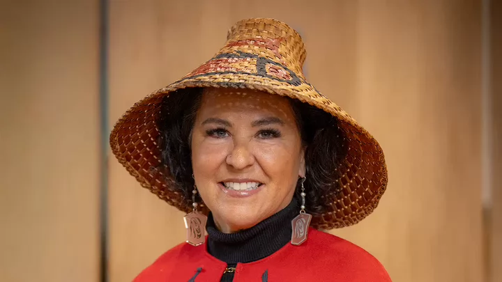 A woman wearing a woven Indigenous hat, dangling earrings and shawl. 