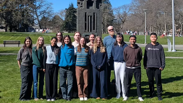 A professor standing among his university students on a campus lawn.