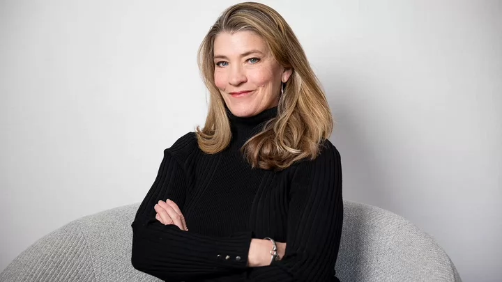 Woman with long straight hair wearing a black turtleneck sweater crossing her arms and smiling.