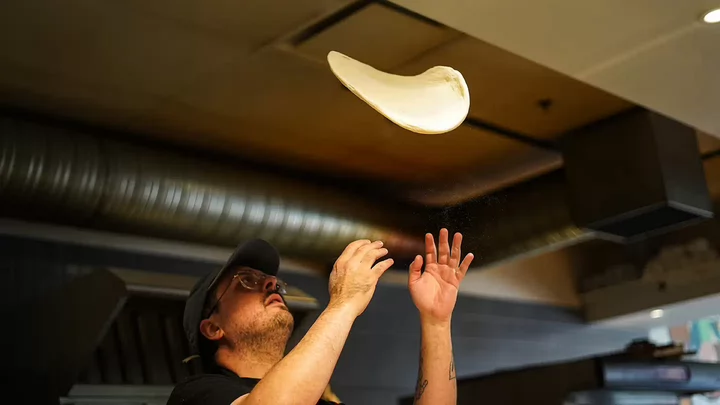 A kitchen worker tosses pizza dough in the air.