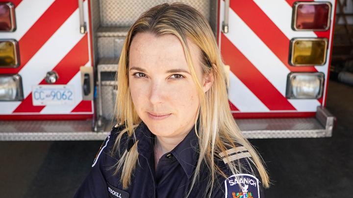 Woman in uniform standing with arms crossed in front of a fire truck.