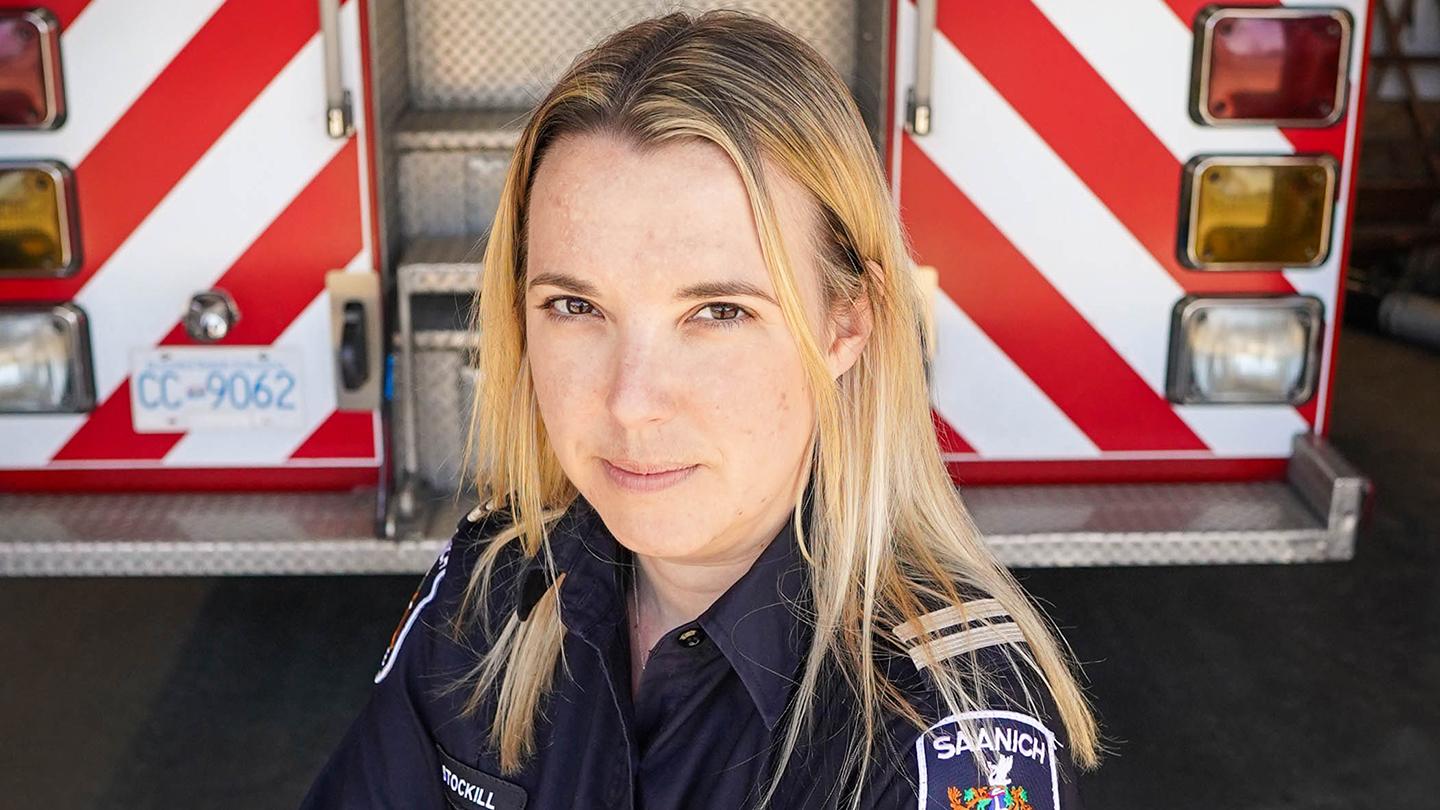 Woman in uniform standing with arms crossed in front of a fire truck.