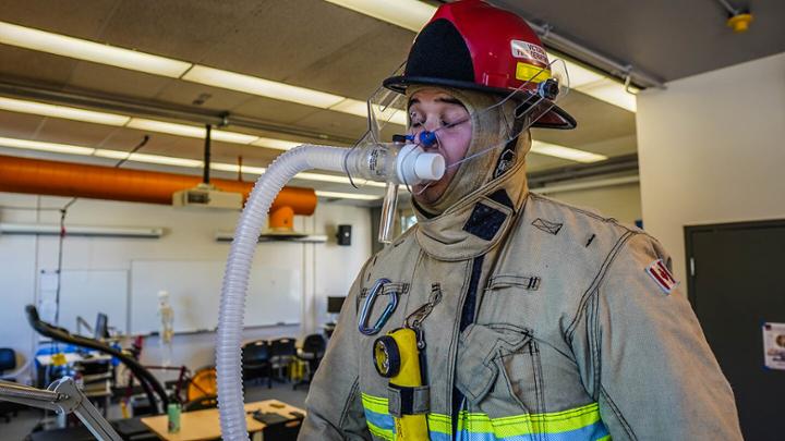 Firefighter in full gear looking tired with breathing hose attached to mouth and nose.