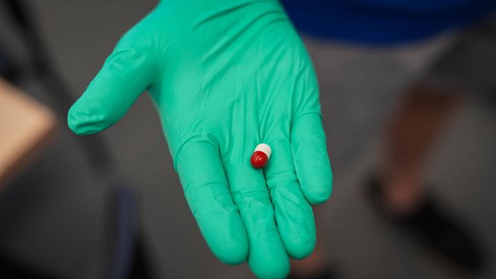Hand with green surgical gloves holds a capsule.