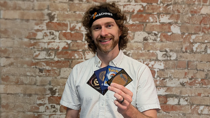 Man wearing a headband that rads TCG Machines standing in front of a brick wall holding an assortment of Magic: The Gathering trading cards.