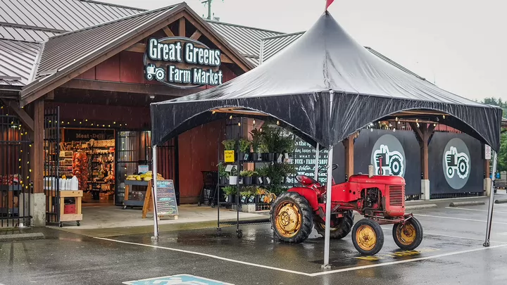 Outside of a grocery store featuring and old tractor and a sign that says Great Greens.