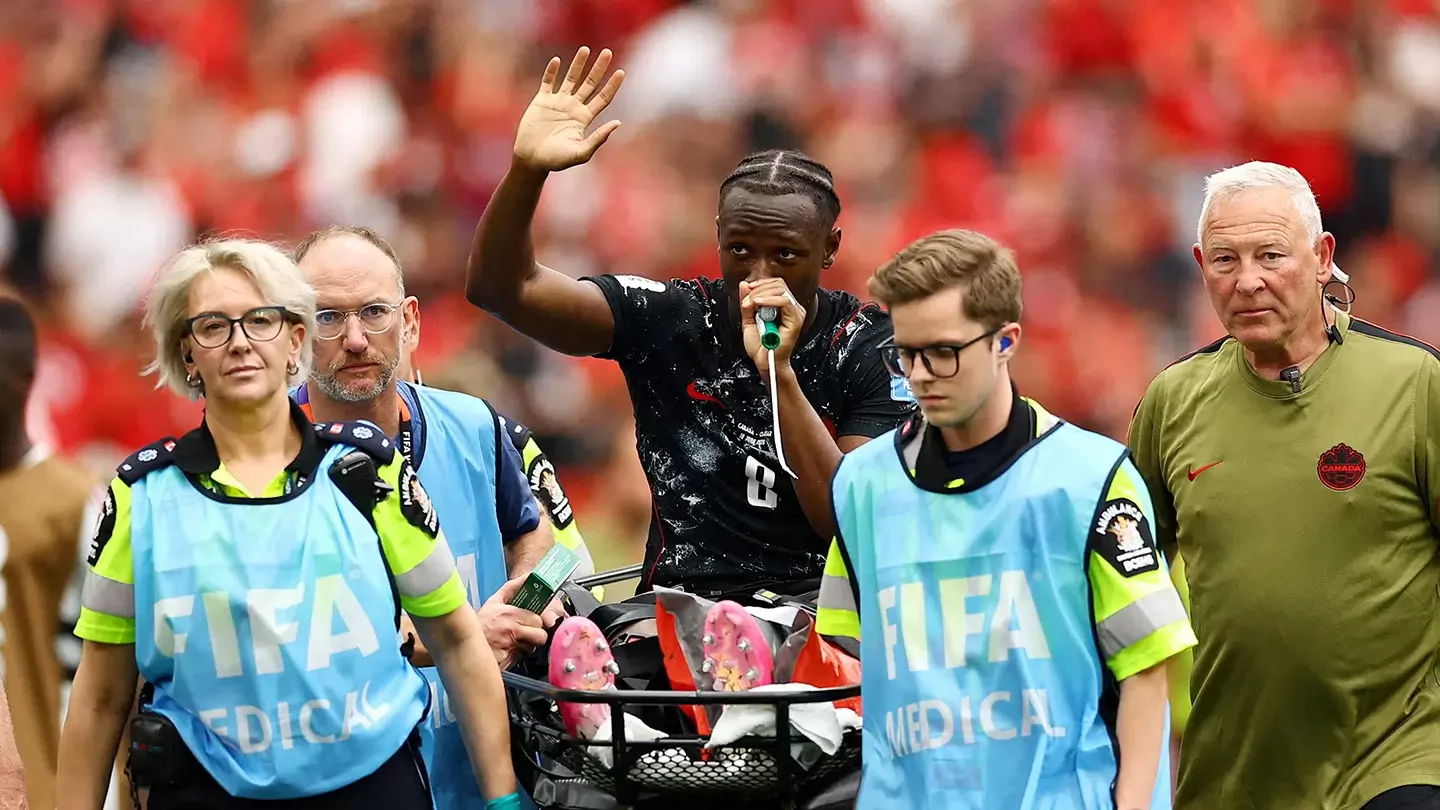 Team Canada soccer player waves to the crowd during World Cup match while being carried off the field on a stretcher. 