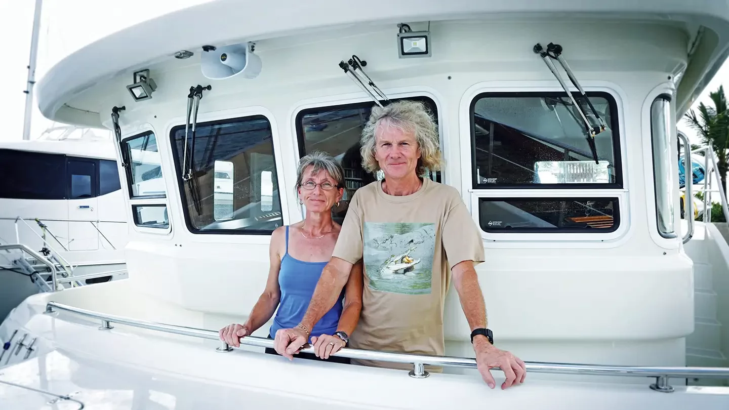 A man and a woman stand on the bow of a yacht while docked. 