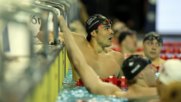 Man in swim cap and swim goggles in a pool looking upwards at end of a race.