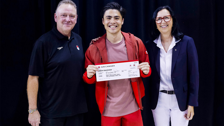 Man holding up Air Canada Ticket to Paris Olympics, smiling while flanked by to people, also smiling.