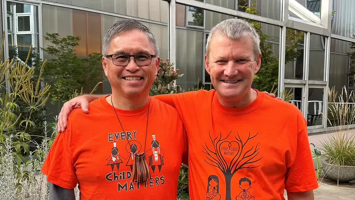 Two men wearing orange Every Child Matters T-shirts standing together arm in arm.