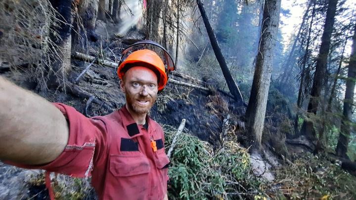 Man with soot on his face standing in a smoky forest charred by wild fires.
