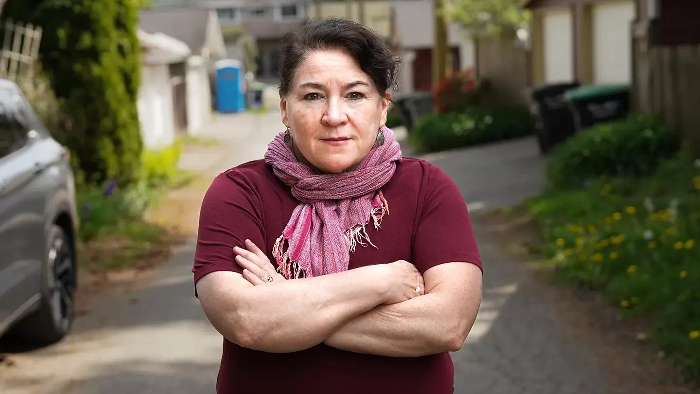 A woman wearing a scarf standing in an alley with her arms crossed. 