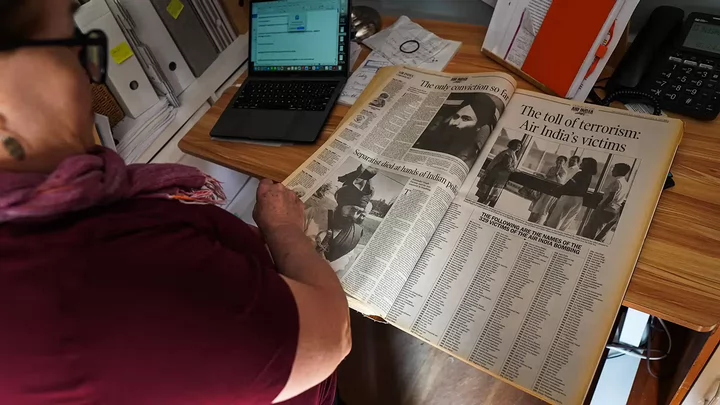 A woman looking at a newspaper with the headline The Toll of Terrorism: Air India's Victims.