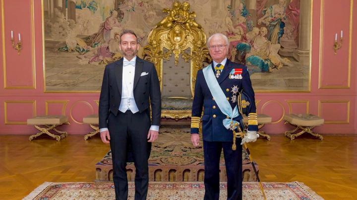 Two men stand in front of golden throne.