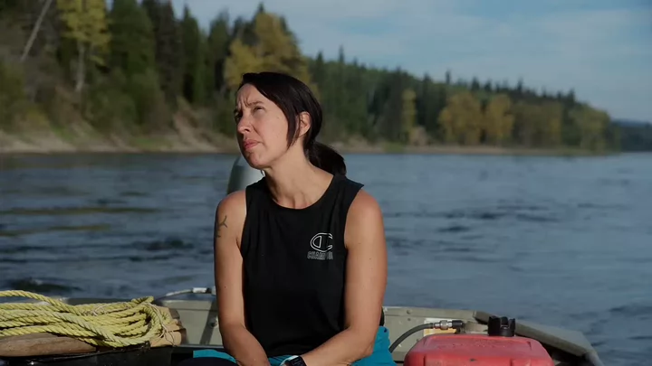 A woman wearing a sleeveless T-shirt sitting on a boat floating on a river looking upward.