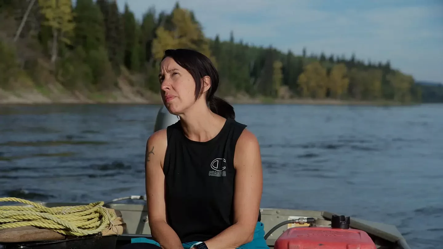 A woman wearing a sleeveless T-shirt sitting on a boat floating on a river looking upward.