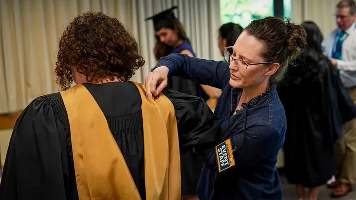 Robing volunteer Mandy Pearce helps a university graduate with their cap and gown.