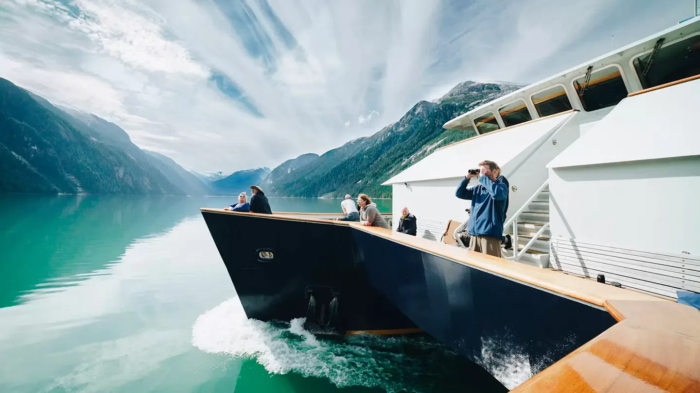 Passengers on the deck of a boat take in the views of mountainous inlet.